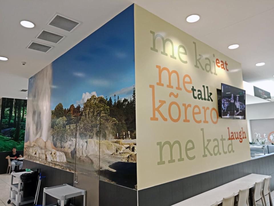Bilingual wall decal at mall reading kai - eat, kōrero - talk and kata - laugh